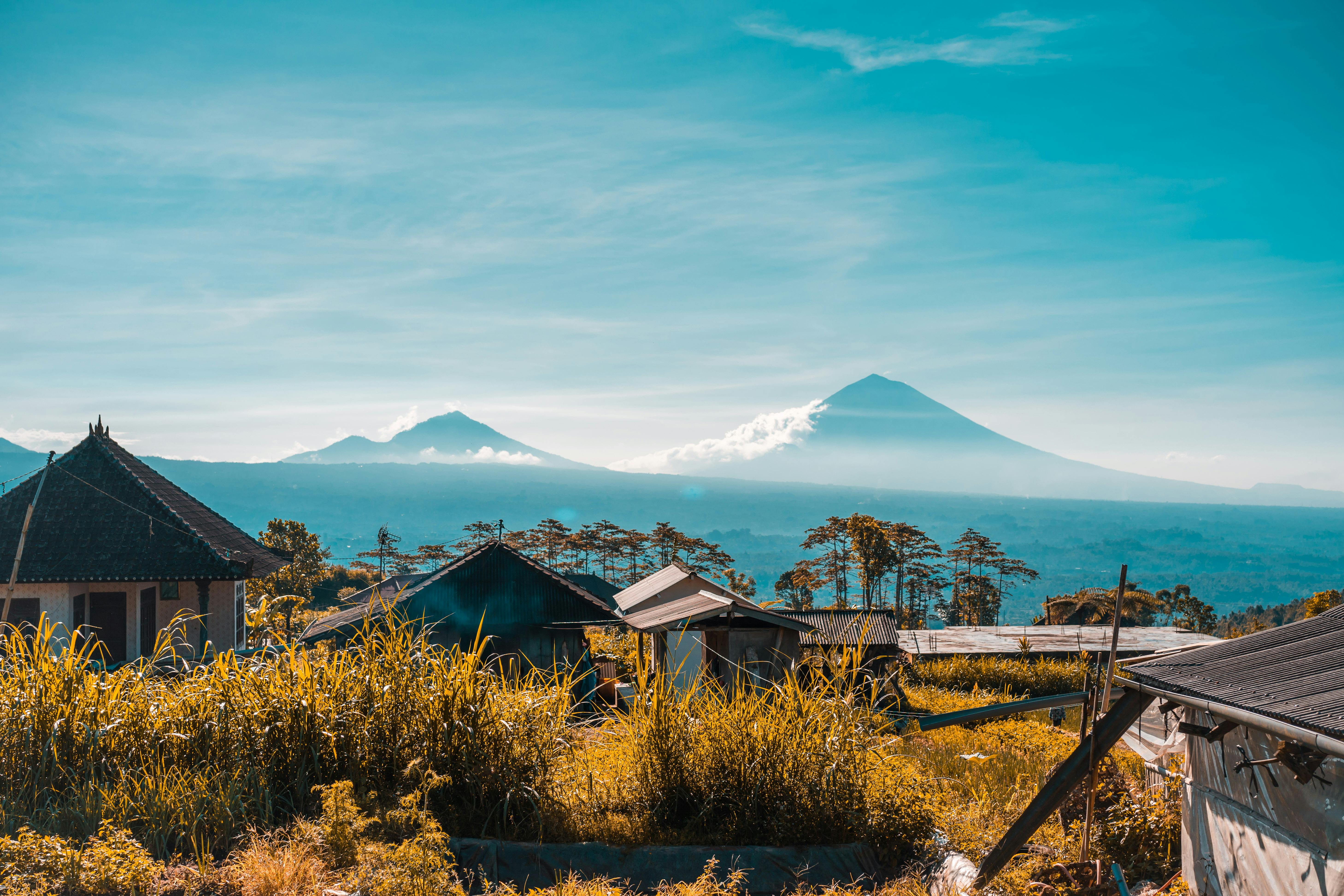 Traditional Balinese village houses with Mount Agung and Batur in the distance under clear tropical skies